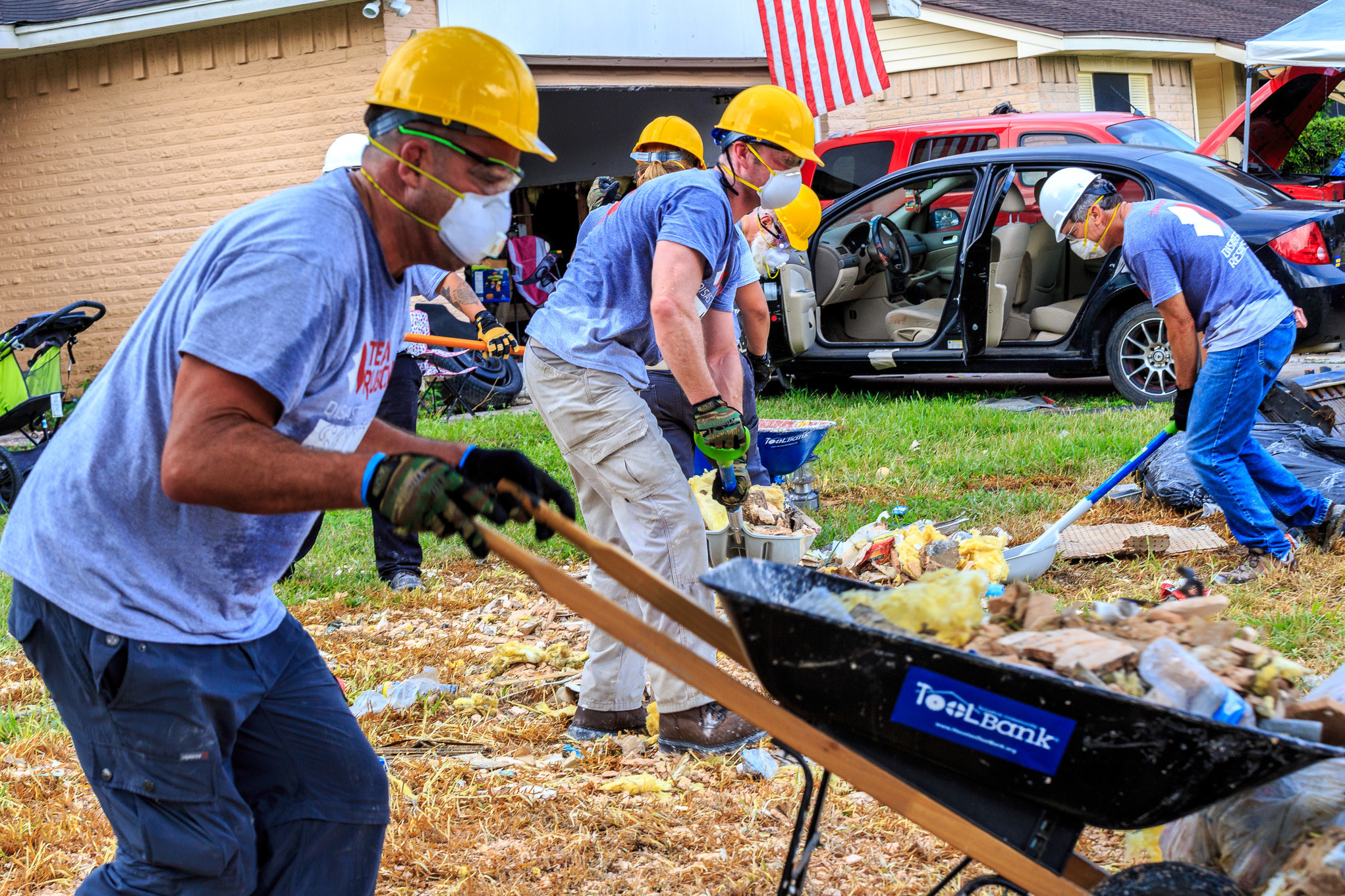 A Team Rubicon volunteer dumps a wheelbarrow full of debris on a debris pile in front of a home 