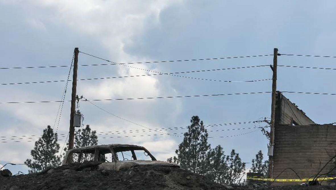 Historic Wildfires Leave Destruction in their Wake -  wires in the sky over a burned-out truck and partial wall