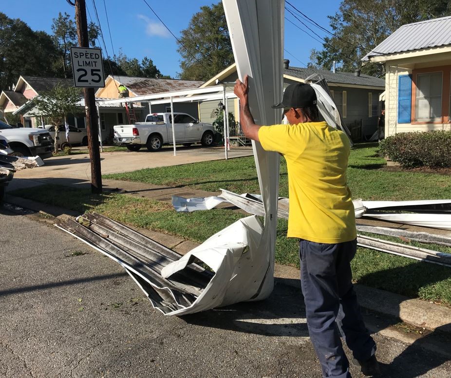 A man in a yellow shirt cleans up large debris on a residential road