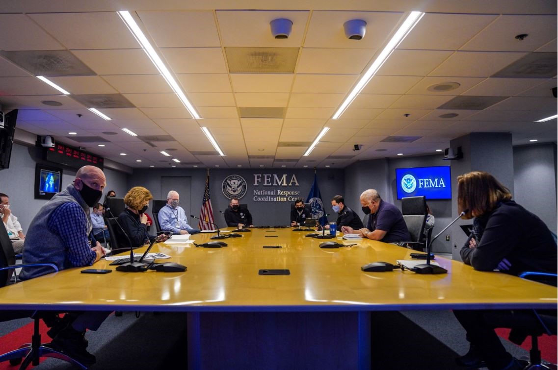 A long conference table with multiple people sitting around it having a conference call