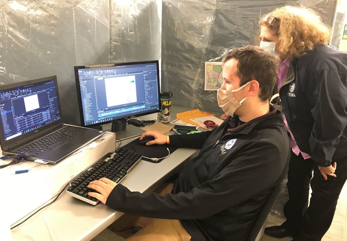 Will Curry (seated), a FEMA geospatial information specialist, provides critical information to Planning Section Chief Toni Knight, in  preparation of Hurricane Delta’s landfall.