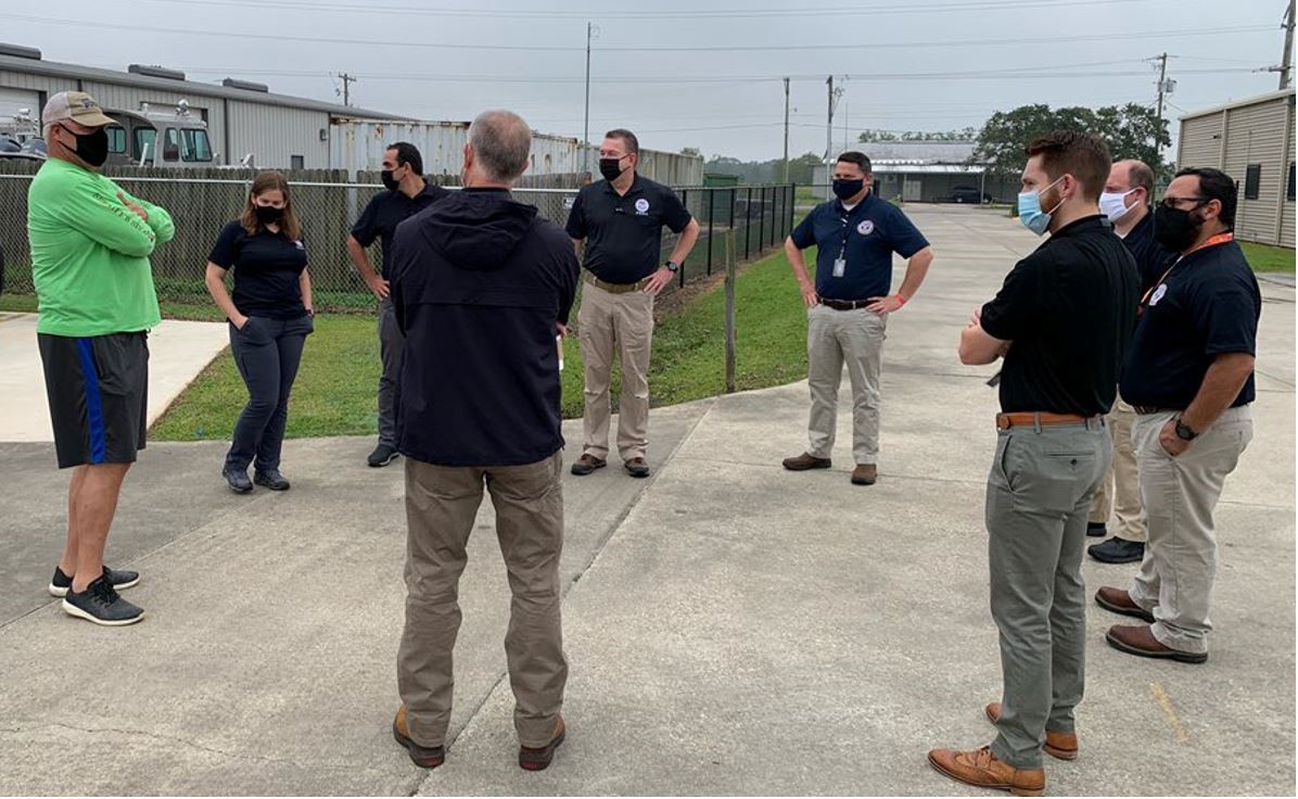 8 men and 1 female all standing in a big circle with mask on talking 