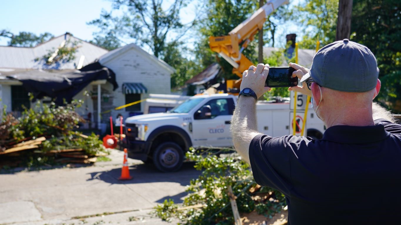 a man standing to the right taking a photo of a house with his phone