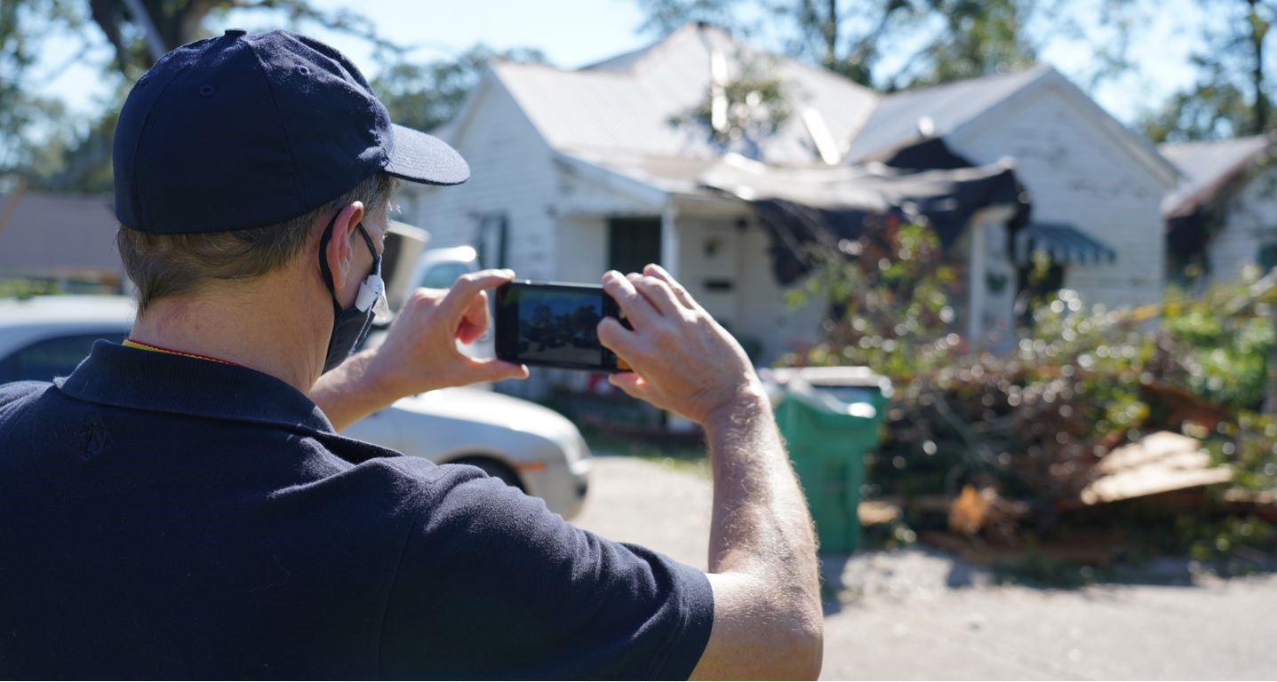 a man standing on the left taking a picture with his phone of a house 