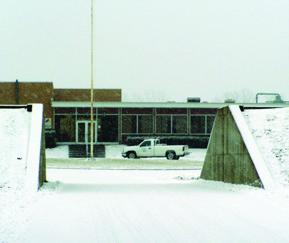 Earthen levee covered in light snow, with an opening for the access road