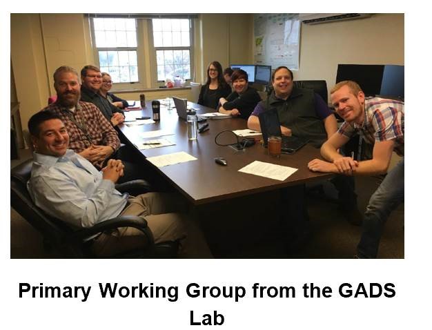 Group of workers sitting around a desk. The text at the bottom reads: Primary Working Group from the GADS Lab. 