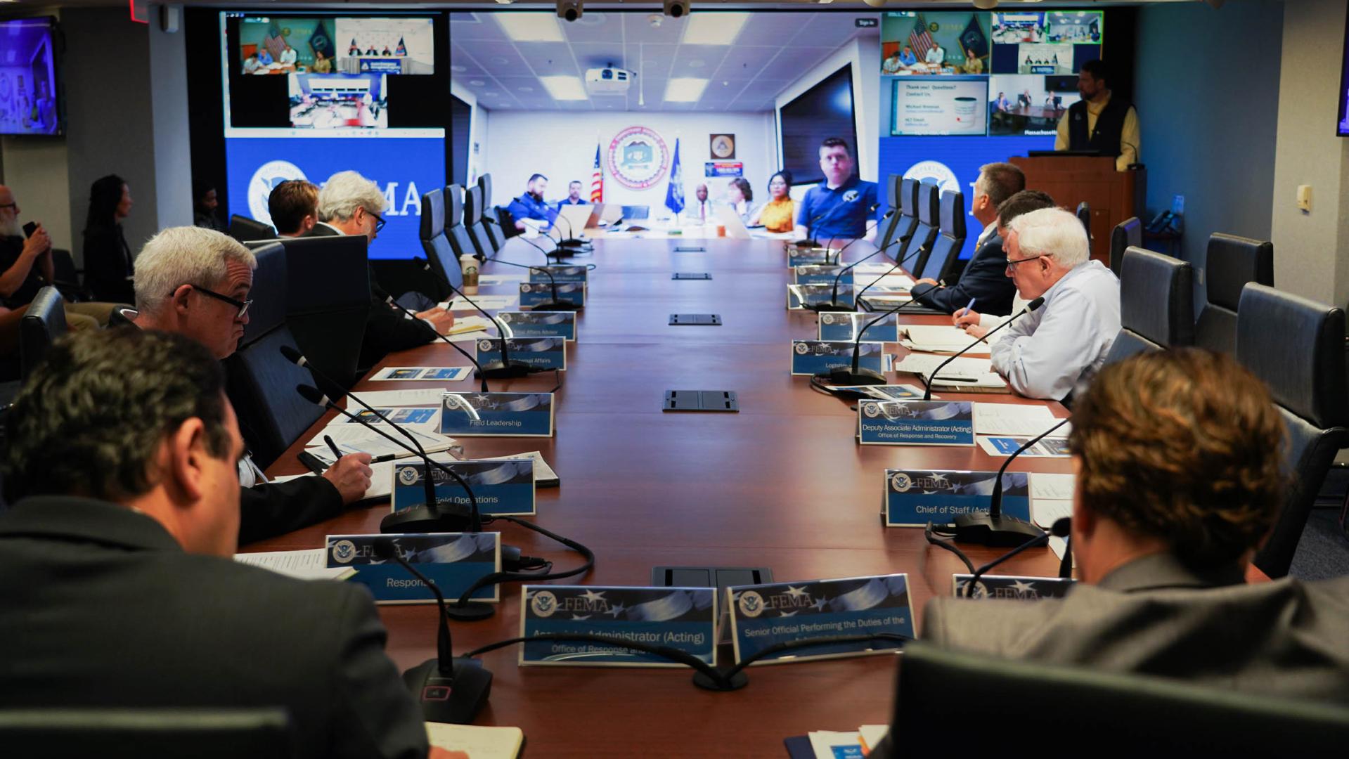 A bunch a people at a table in front of a video conference call.
