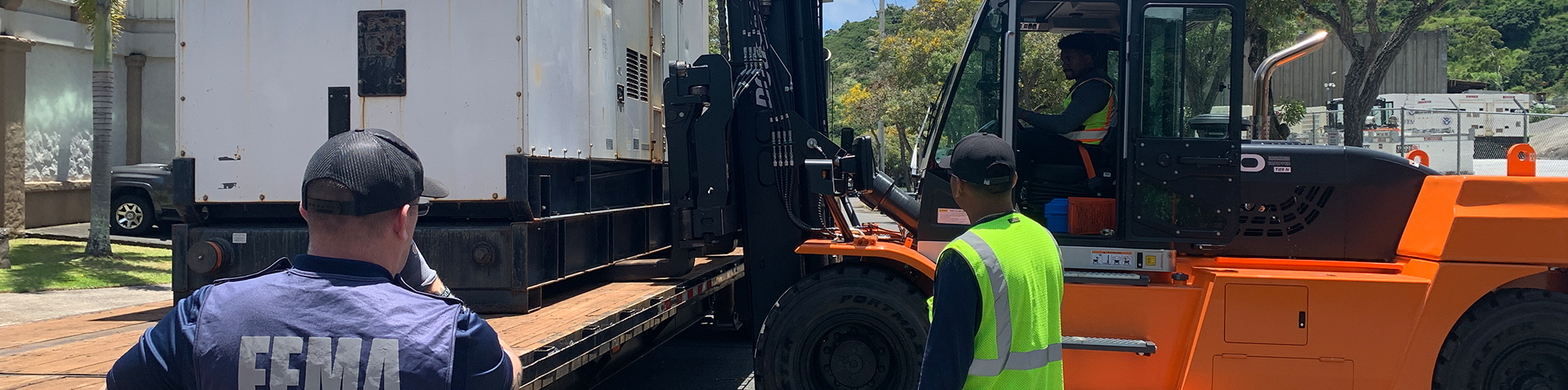 A picture of a FEMA employee and two other people moving a generator using heavy construction equipment