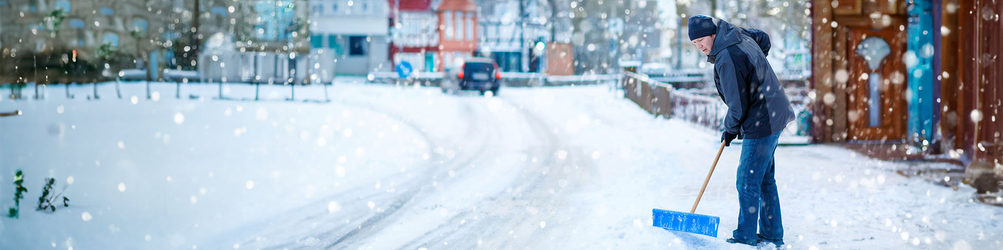 一个男人正在城市的街道清雪。他穿着暖和的衣物，包括帽子和手套。