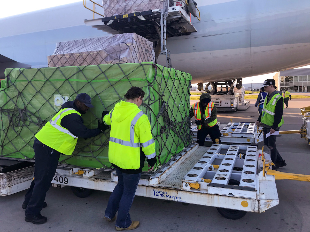 Airport employees position a pallet of medical supplies to transport.