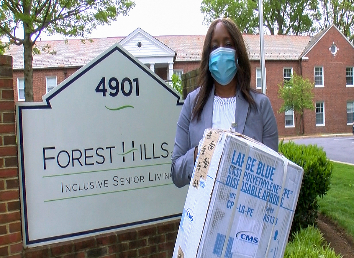 A person stands near a sign holding a box of PPE.