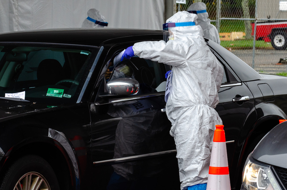 Medical personnel is passing something through a parked car's window.