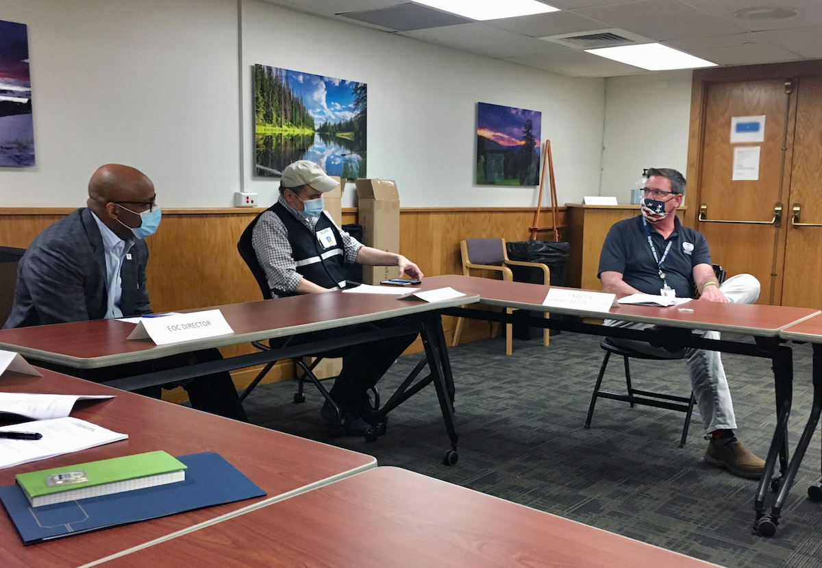 Three people sitting at a table talking, wearing face masks.