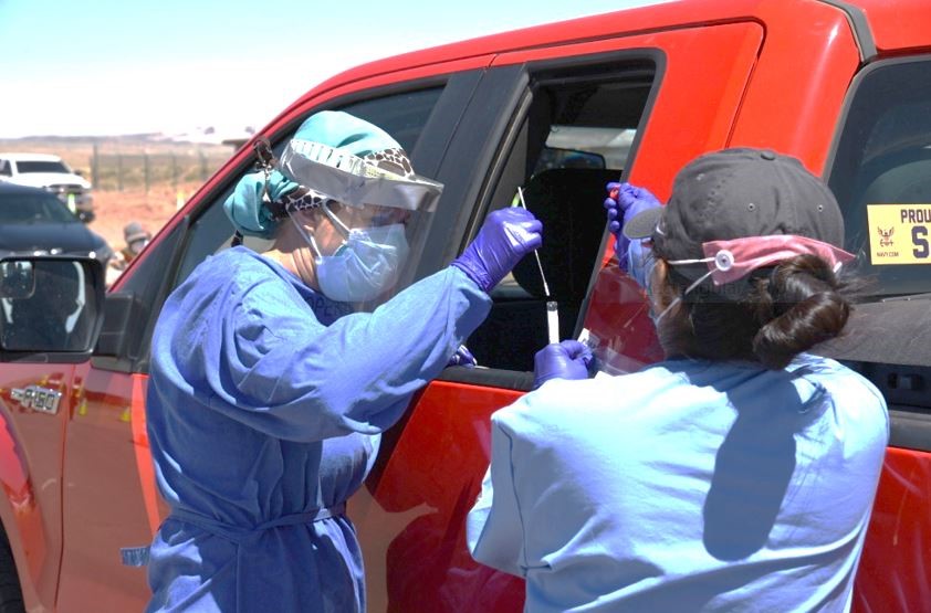 Two female healthcare working doing a COVID-19 test outside beside a big red pickup truck