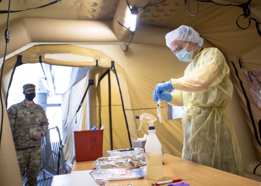 a soldier watching a healthcare professional preparing a specimen bag for a COVID-19 testing vial in a mobile testing center