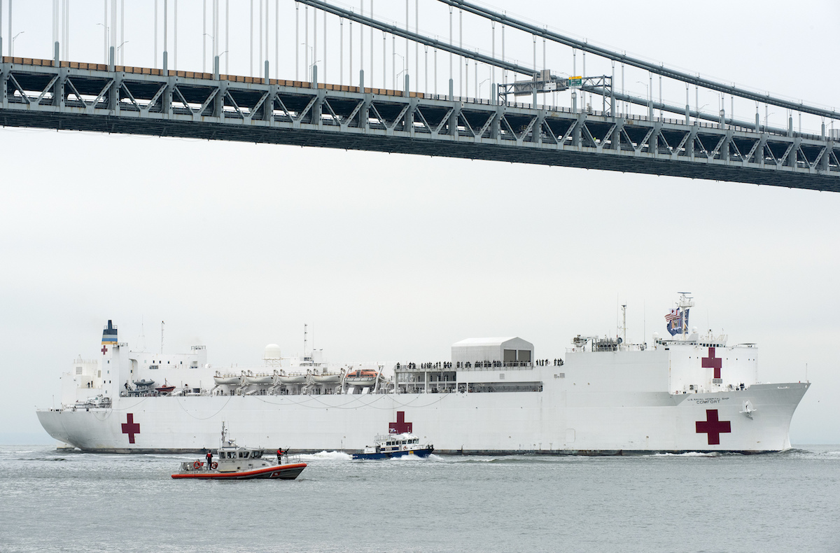 USNS Comfort sails under a bridge escorted by smaller ships.