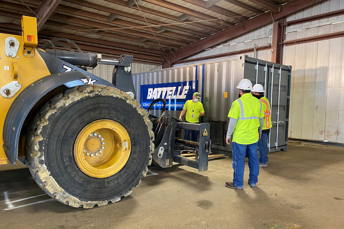 Large machinery delivers a Battelle unit as workmen stand nearby.