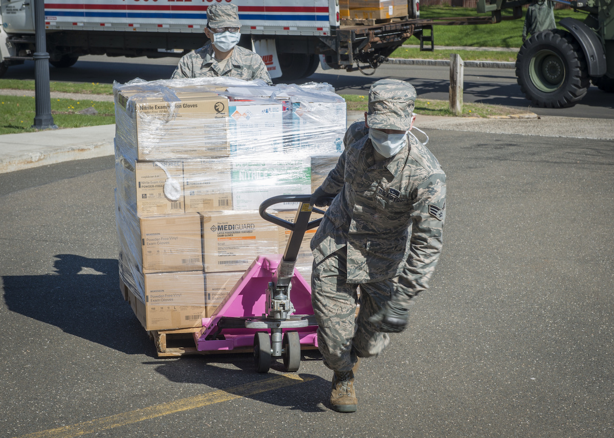 Two soldiers move a pallet truck with PPE.