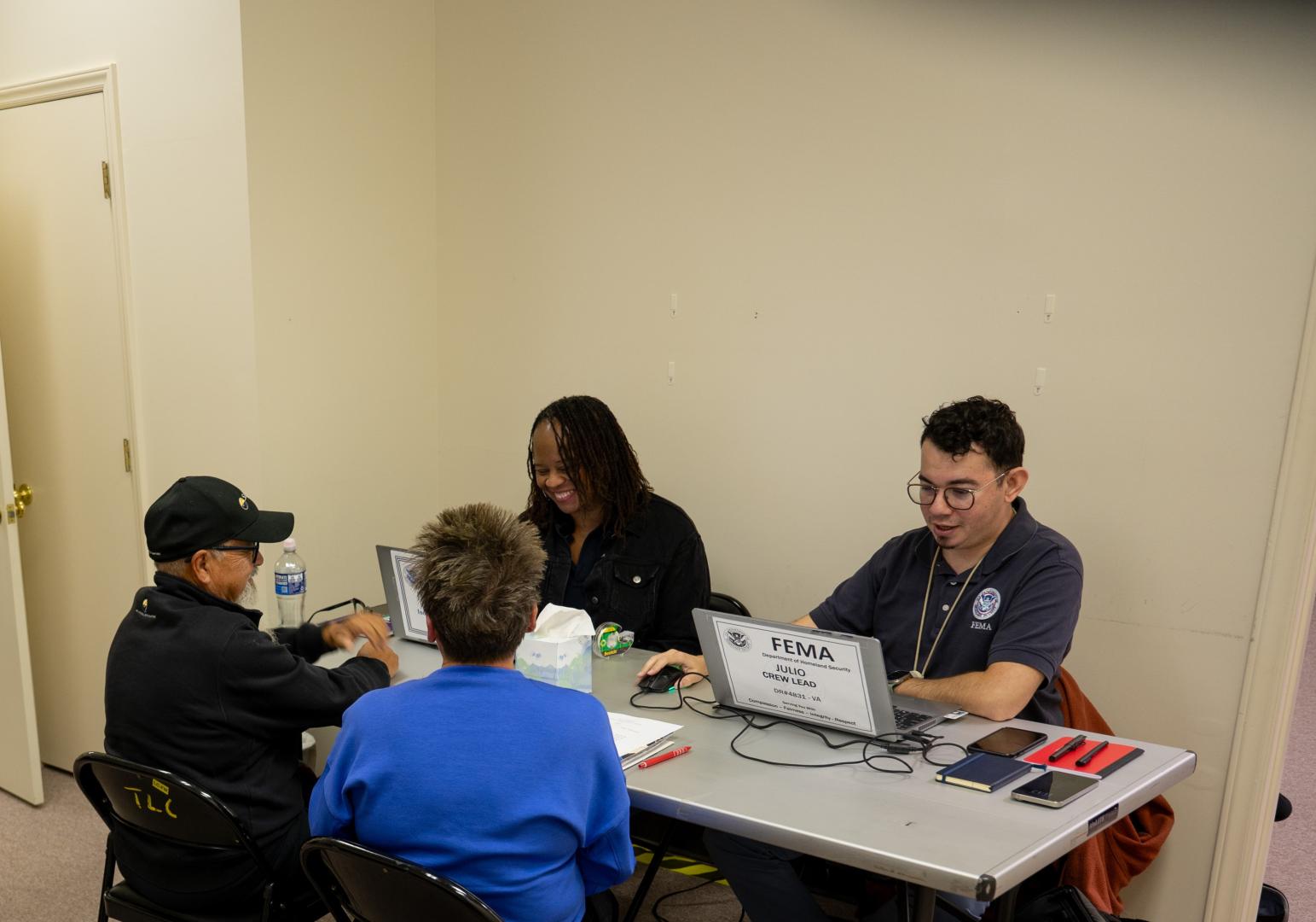 FEMA staff at a Disaster Recovery Center sitting at multiple tables sharing information about FEMA programs with survivors.