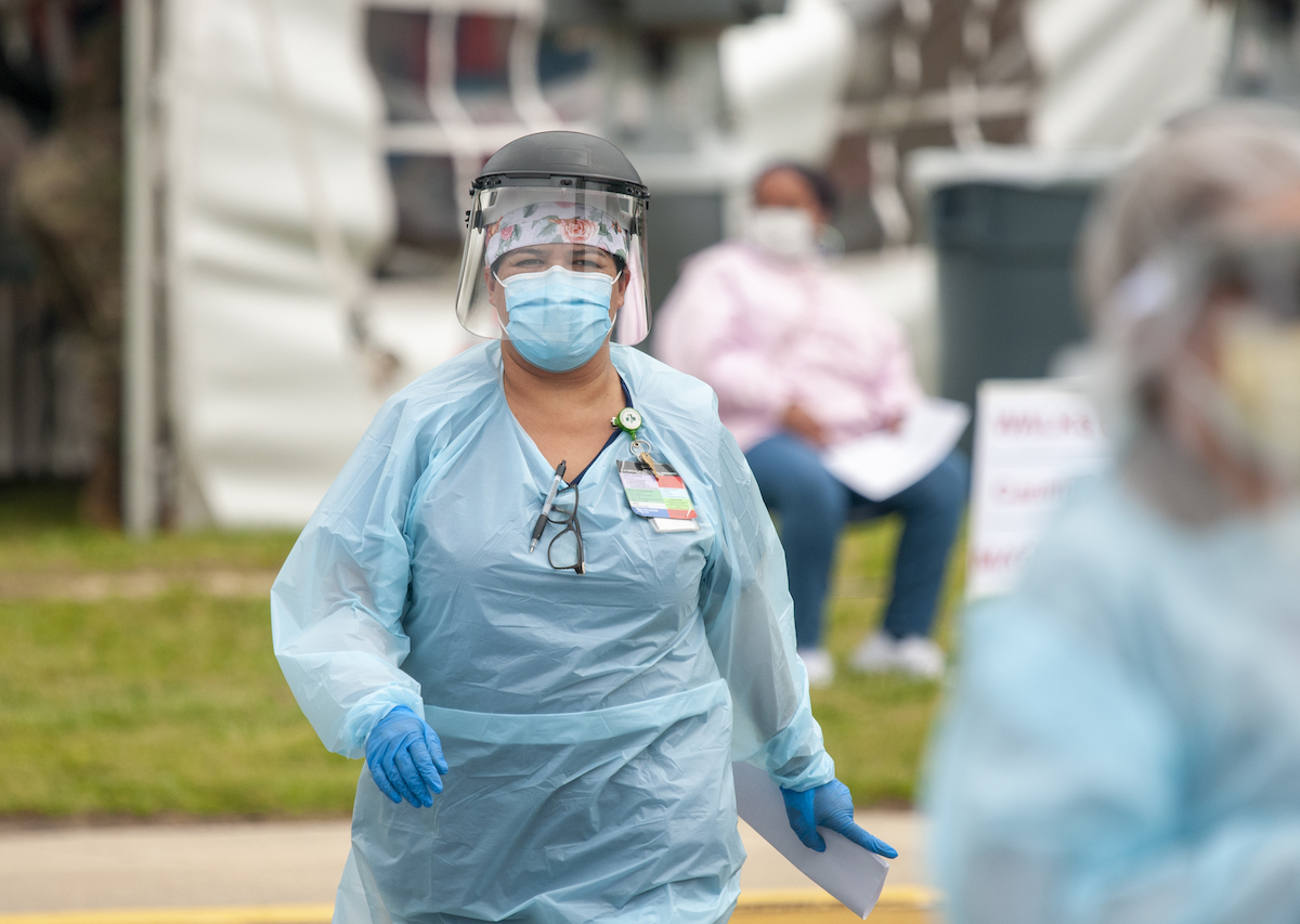 Nurse in full PPE and face shield walking towards the camera.