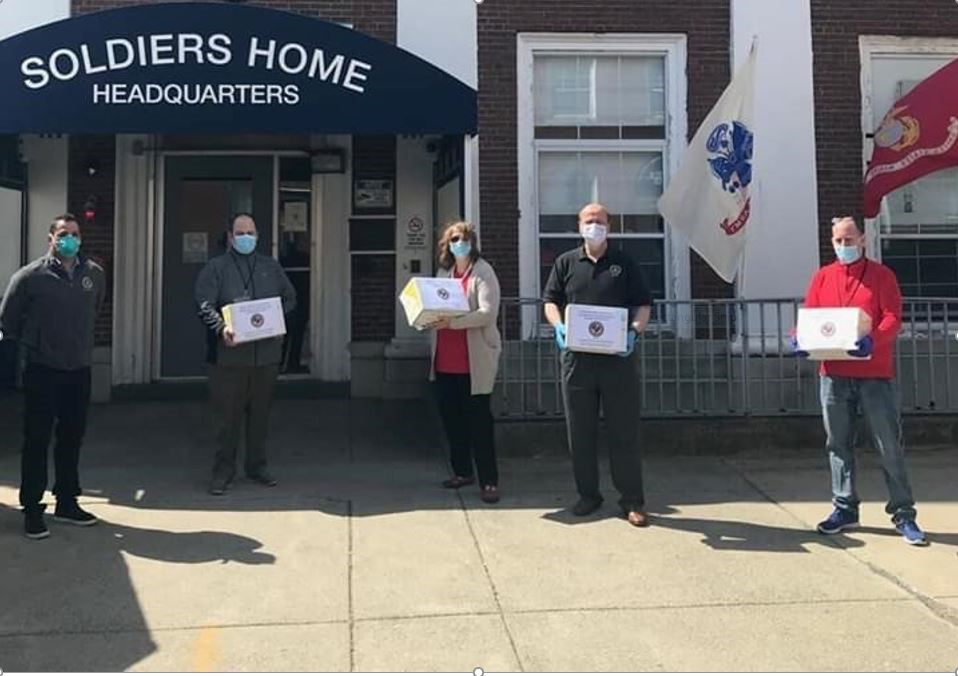 4 males and 1 female standing in front of a building holding boxes