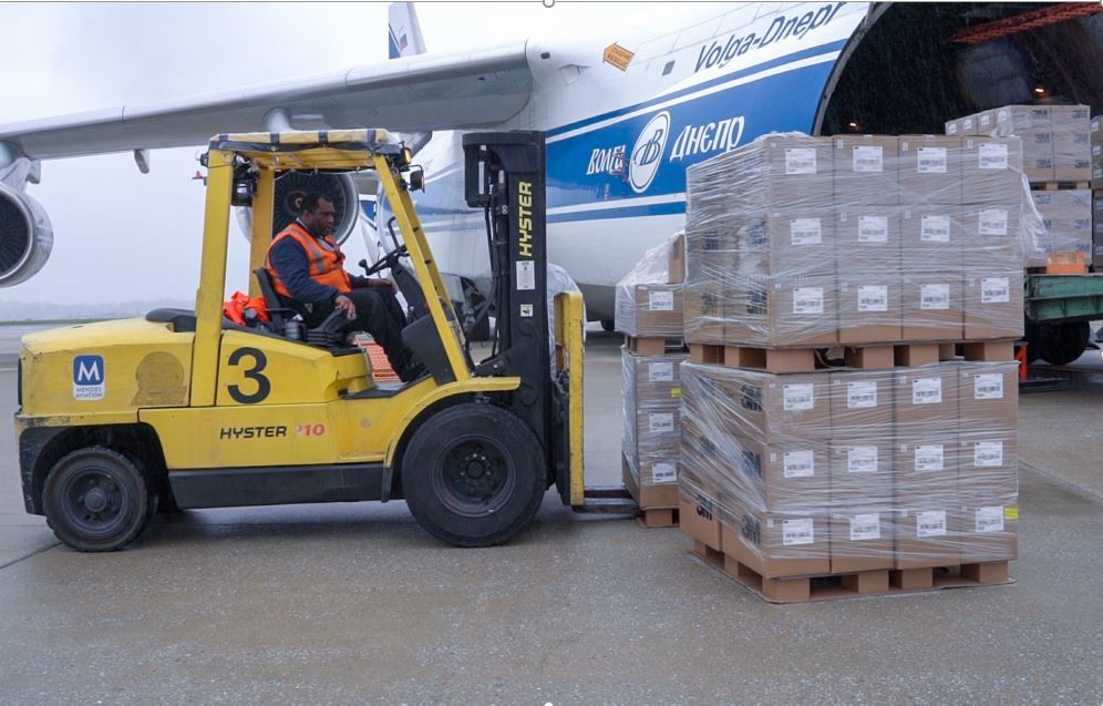 A man riding a forklift, loading crates of boxes on plane