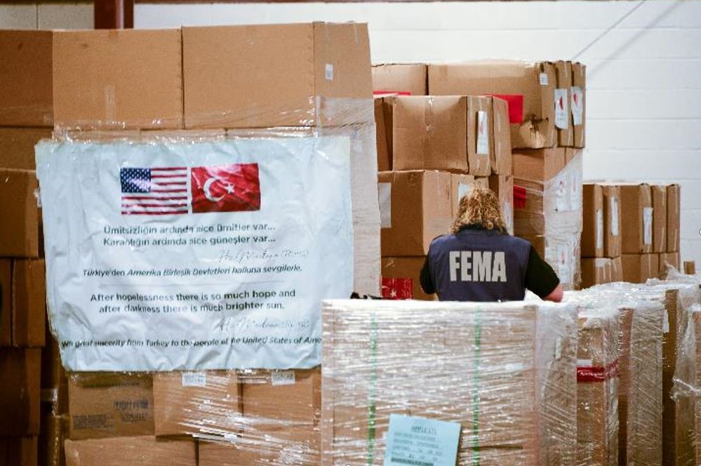 A female FEMA employing going through boxes with her back turned towards the camera with a FEMA vest on