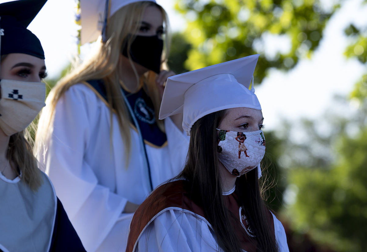Graduates standing in cap and gown and PPE masks.