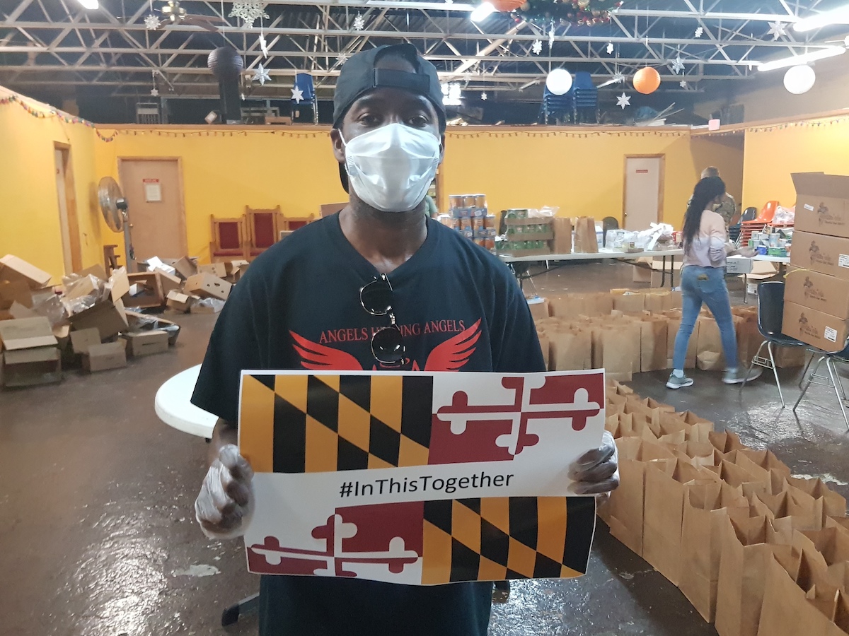 Man in PPE holds up a MD sign that has a MD flag image and the words #InThisTogether