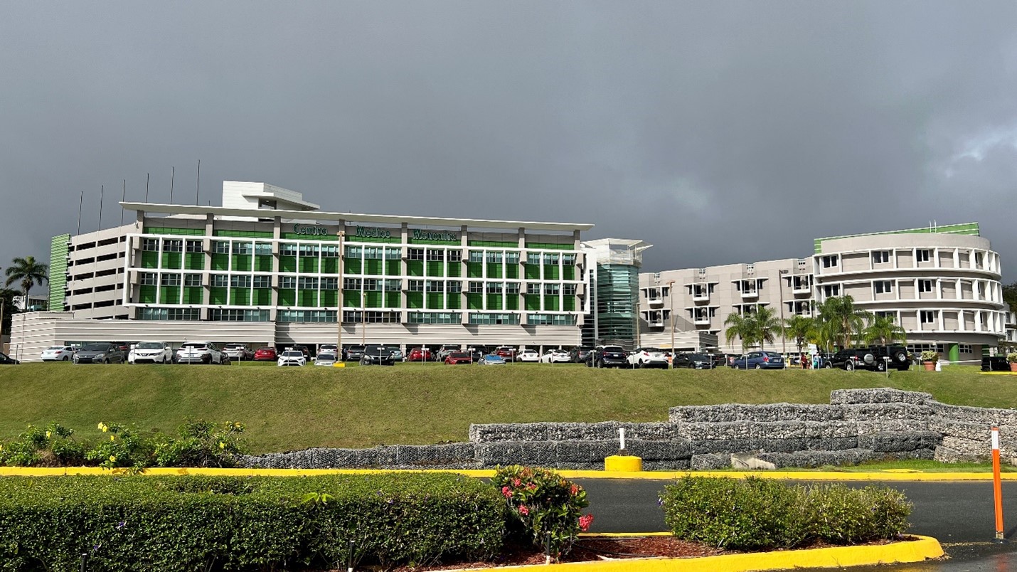 View of the Mennonite Ganeral Hospital buildings. At the right, three strory building with big glass windows. At the right, three story grey building with small square windows.