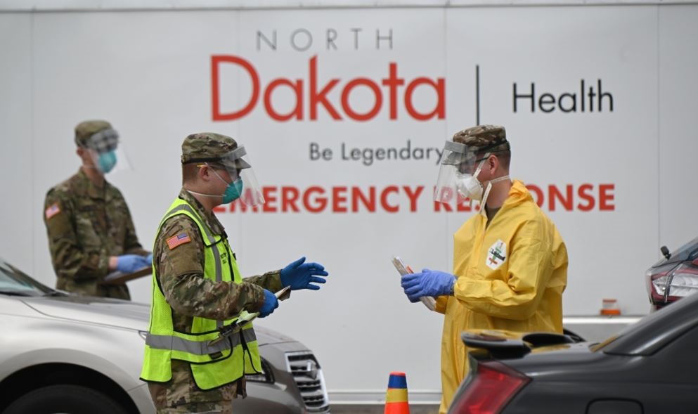 soldiers with mask on, standing outside talking while surrounded by cars