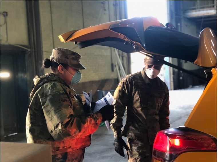 One female soldier and one male soldier looking into the trunk of a car.