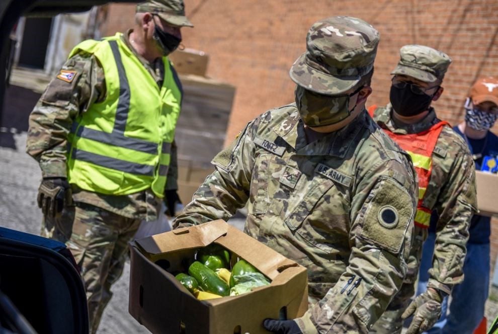 Male soldiers putting veggies in the trunk of a car