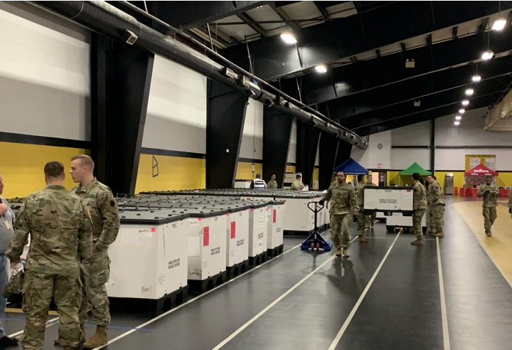 8 male soldiers in a gym unloading federal equipment and talking