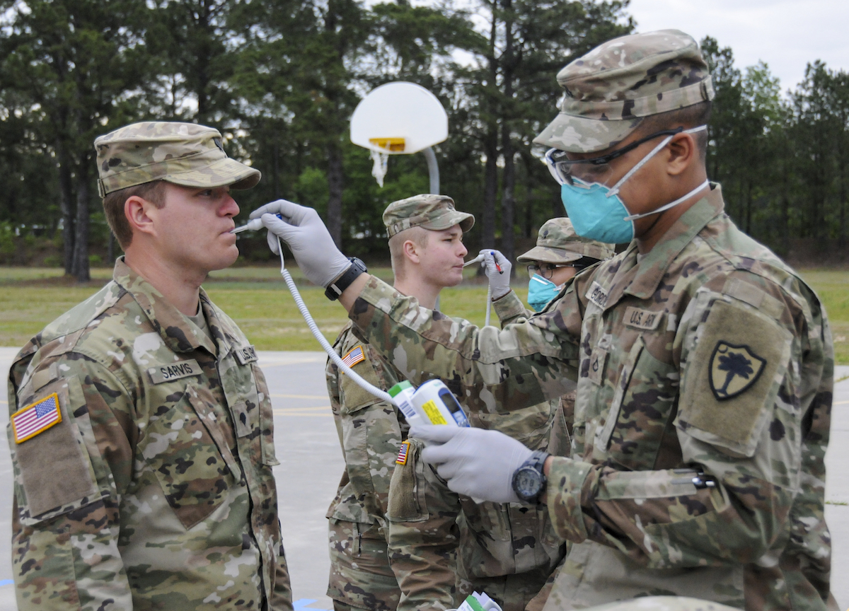 People in military uniforms are doing medical tests on one another. It seems that one person is taking another person's temperature. 