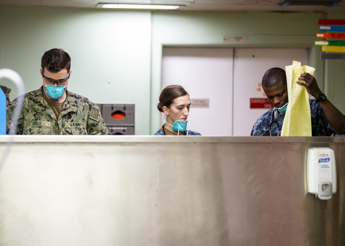 Navy Medical personnel don protective gear to treat patients.