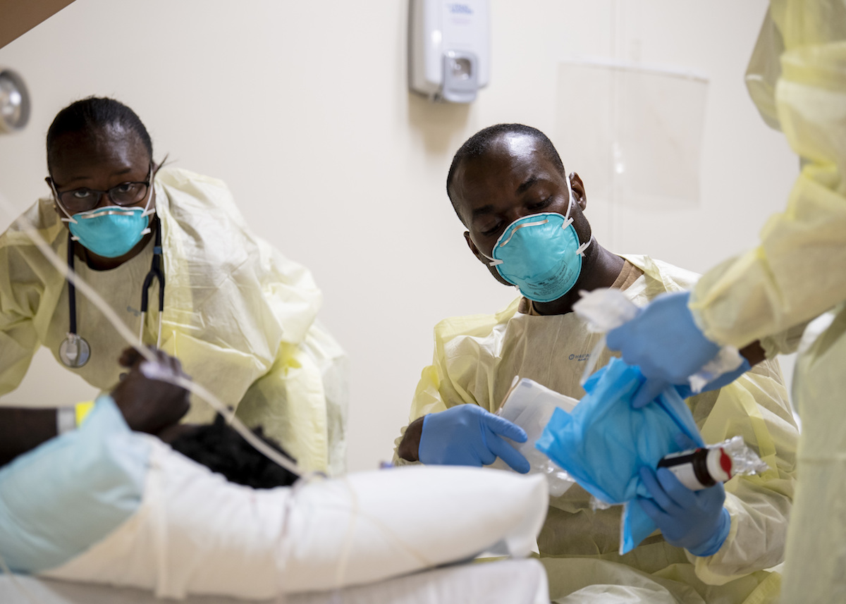 Medical personnel in masks and gowns pass bloodwork and supplies to a third person.