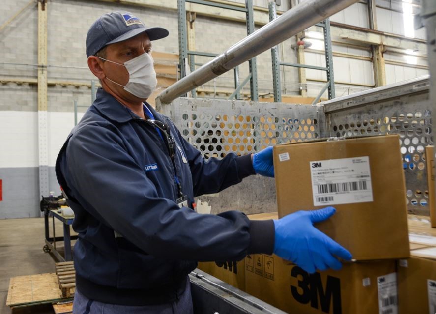 A male Postal Service worker loads boxes of respirators and masks for shipping