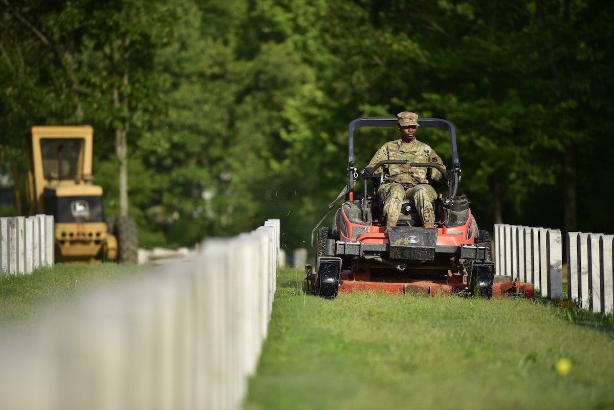Military man riding a lawn mower in between rows of gravestones at a VA cemetery.