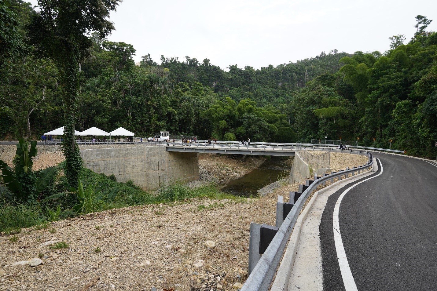Vista de carretera y puente recién reconstruidos. Tres carpas blancas pueden ser vistas al final de la carretera.