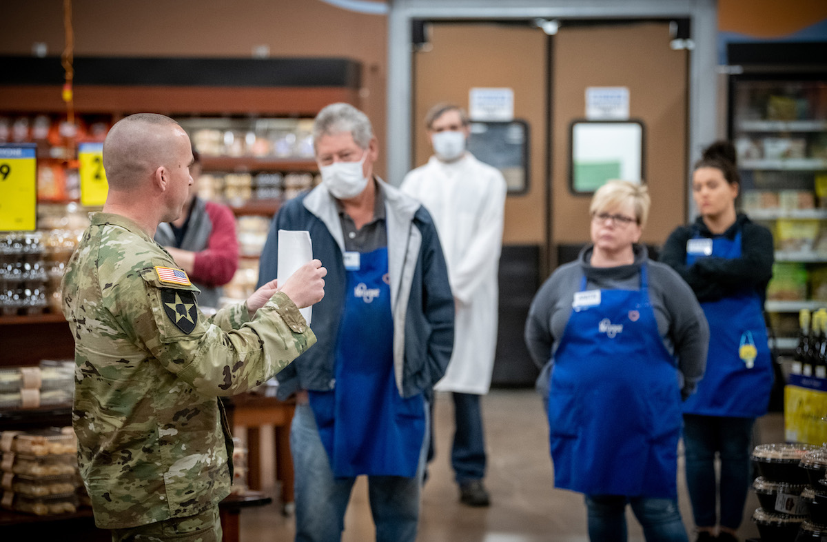 A soldier holds up a piece a paper as he talks to grocery workers in a supermarket.