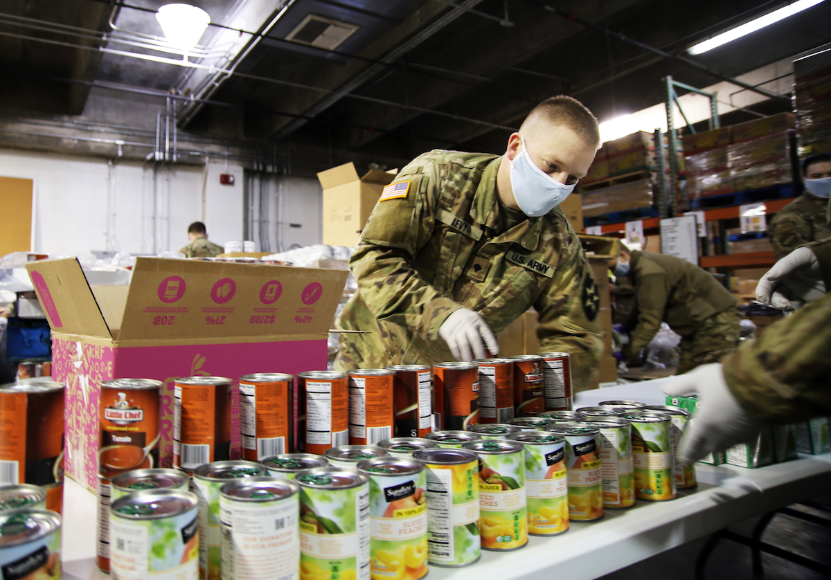 A soldier wearing a face mask puts canned food into a box.