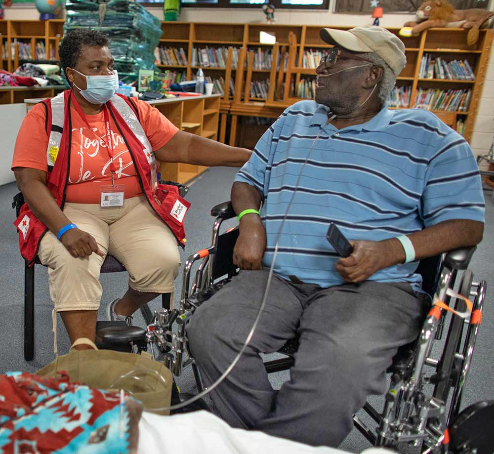 Man sits in wheelchair next to person sitting in red vest.