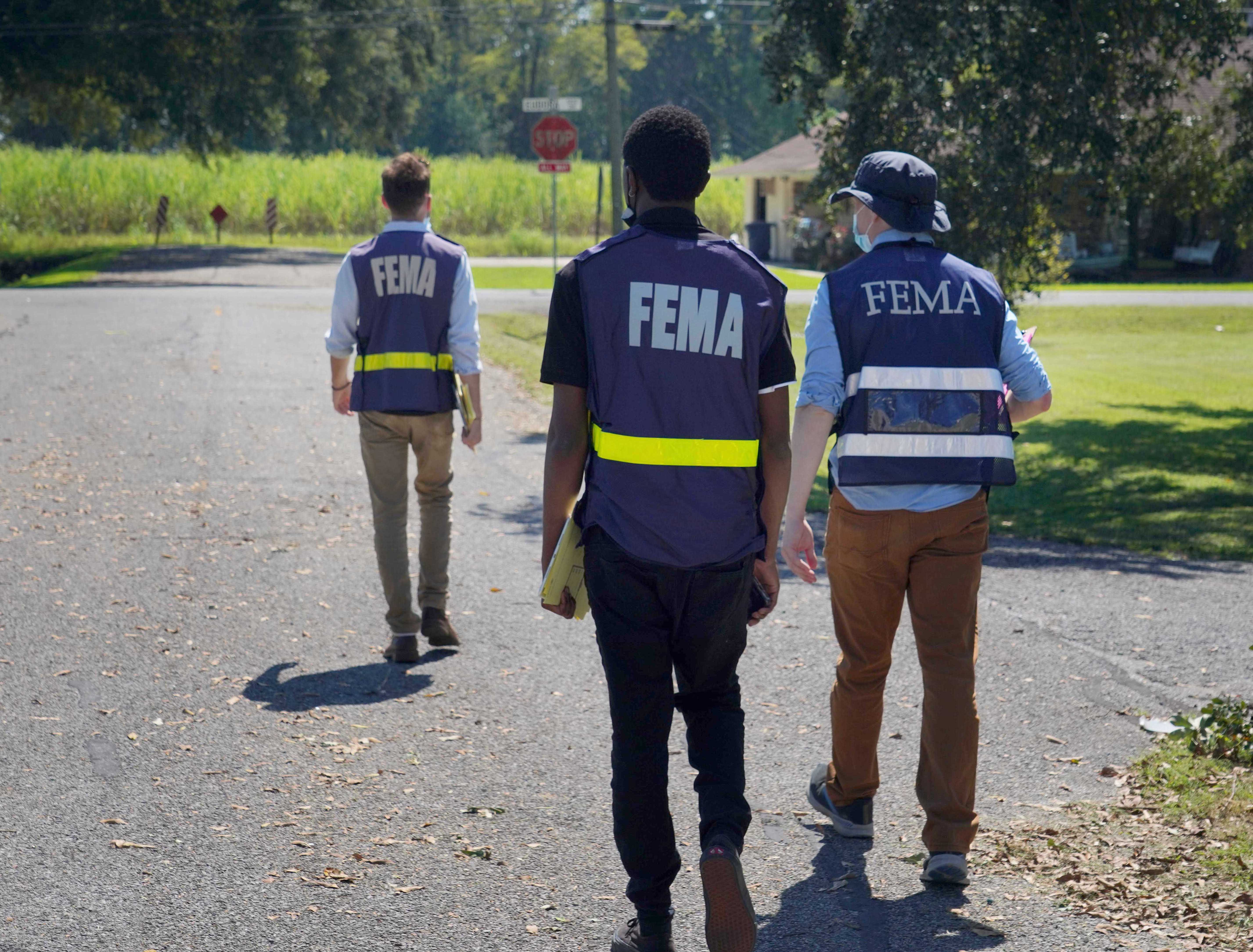 Three people in FEMA vests walk together away from the camera