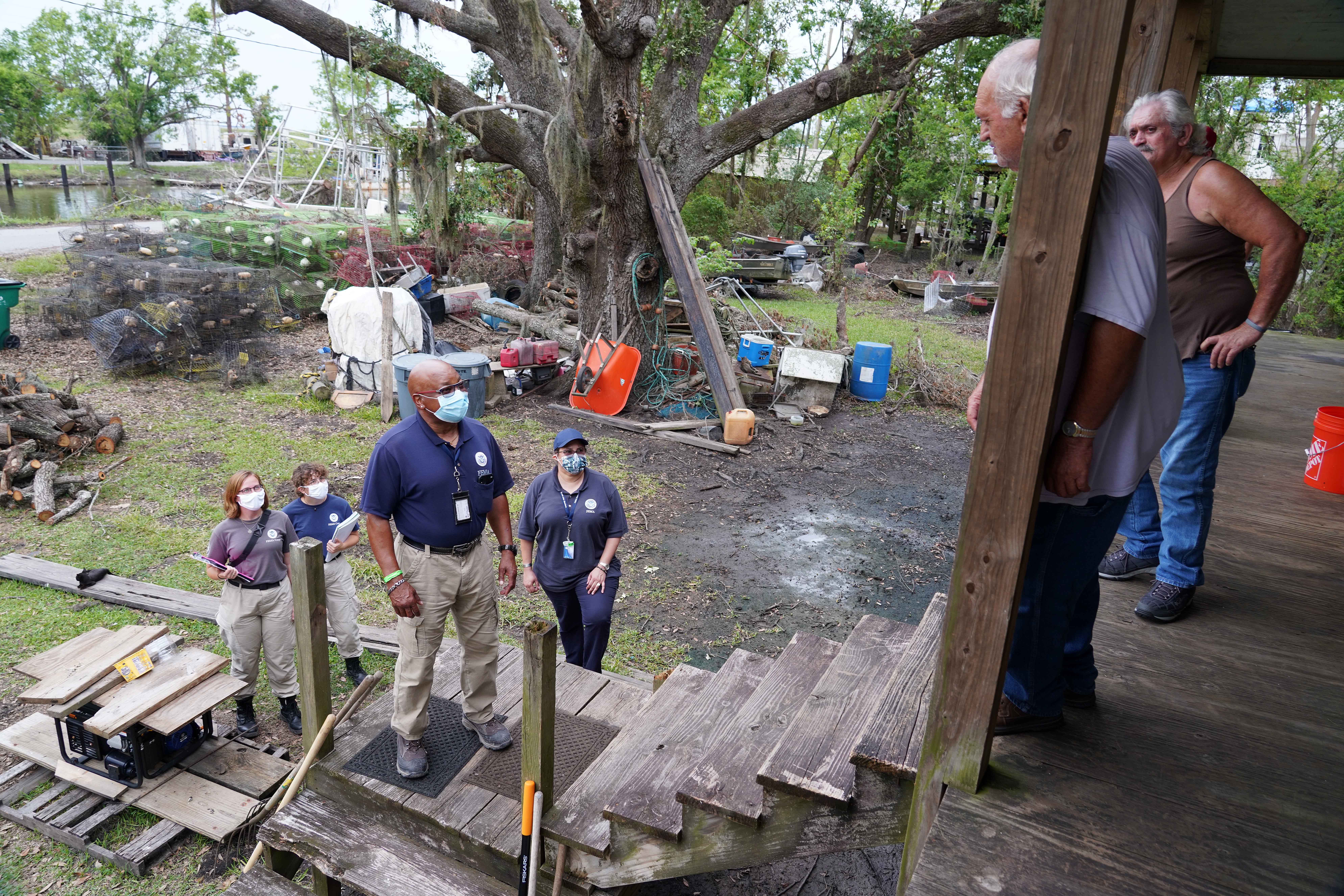 A group of FEMA responders talk to two survivors who are standing on a front porch