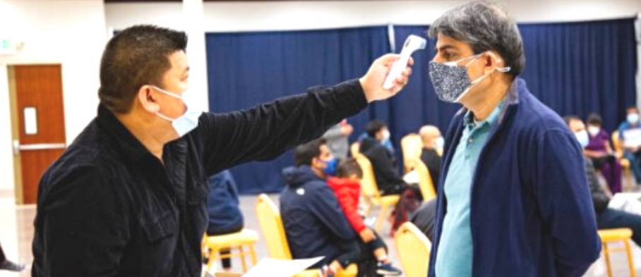 Volunteer checks someone’s temperature at a vaccination site.