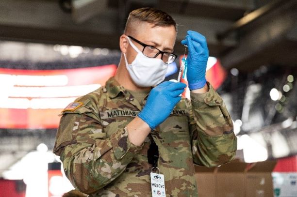 Sgt. Matthew Mattias, a combat medic assigned to to Fort Stewart, Ga., prepares a syringe with the COVID vaccine before administering to a patient in Atlanta’s community vaccination center at Mercedes-Benz Stadium.