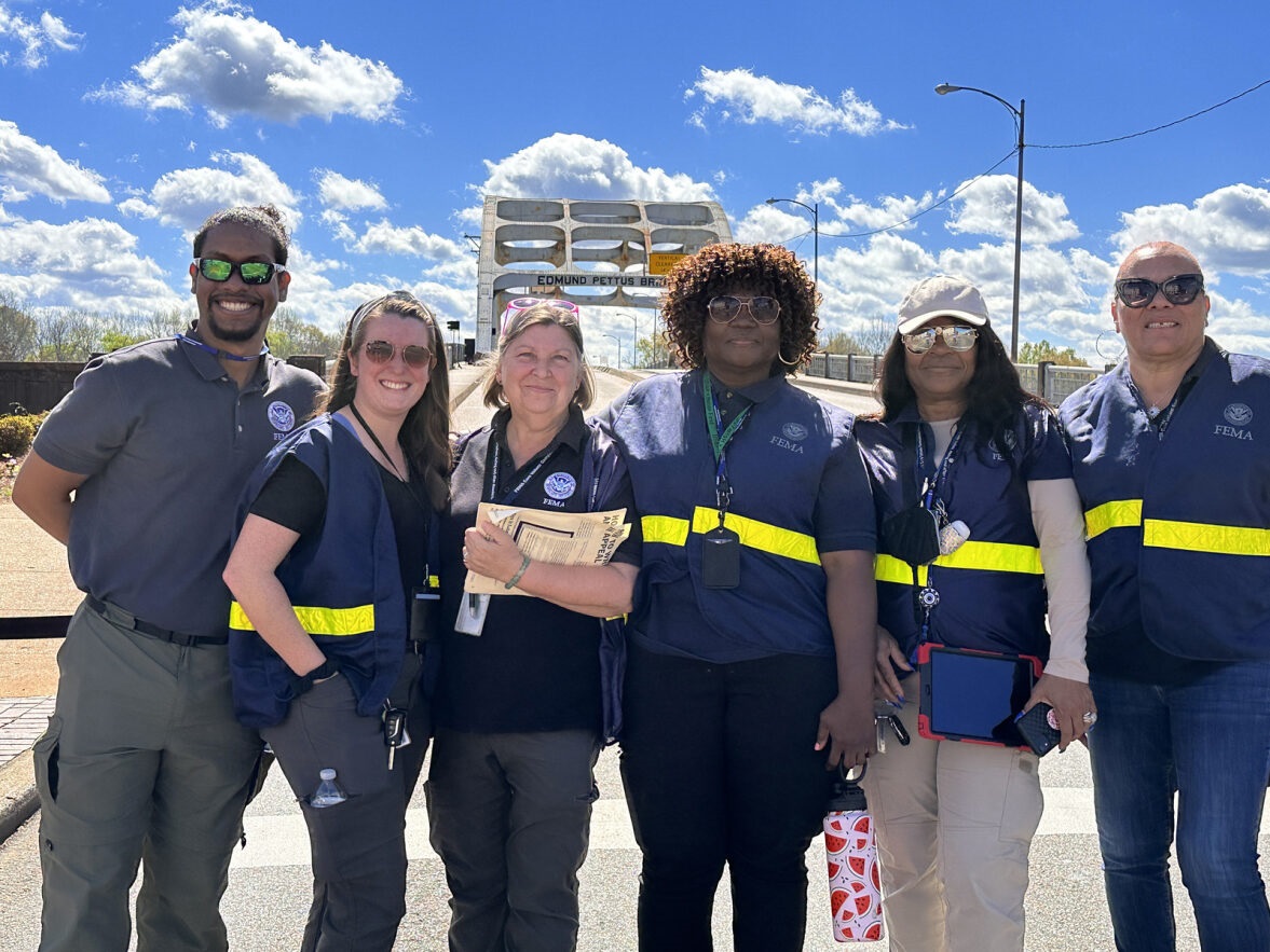 Six FEMA reservists pose in front of a bridge