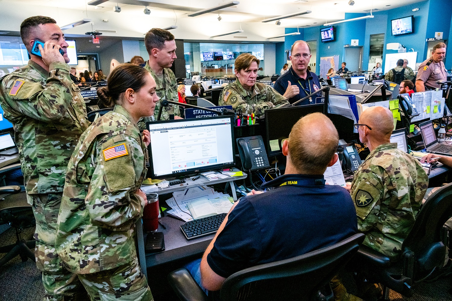 Uniformed military personnel standing around a computer with a FEMA employee.