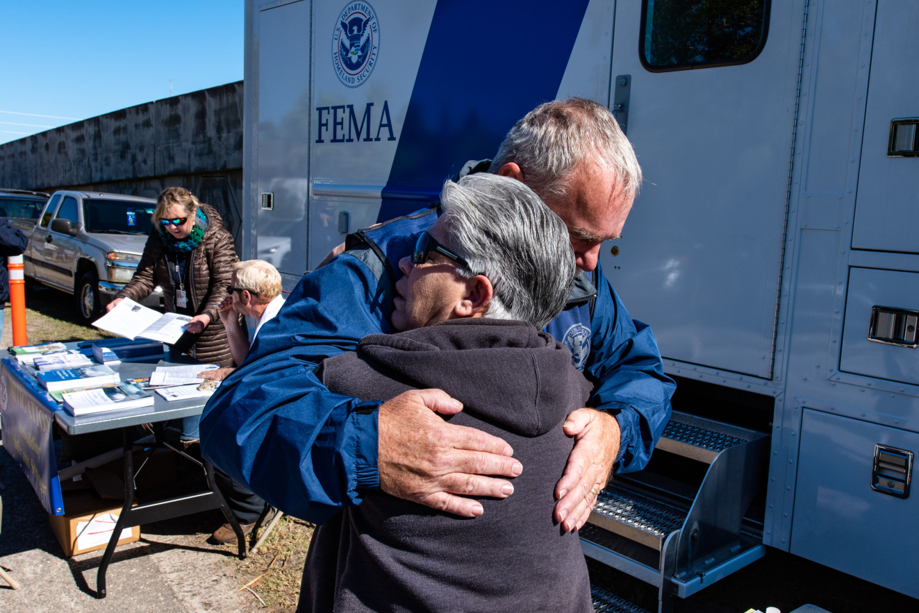 A woman hugging a FEMA employee at a mobile recovery station.